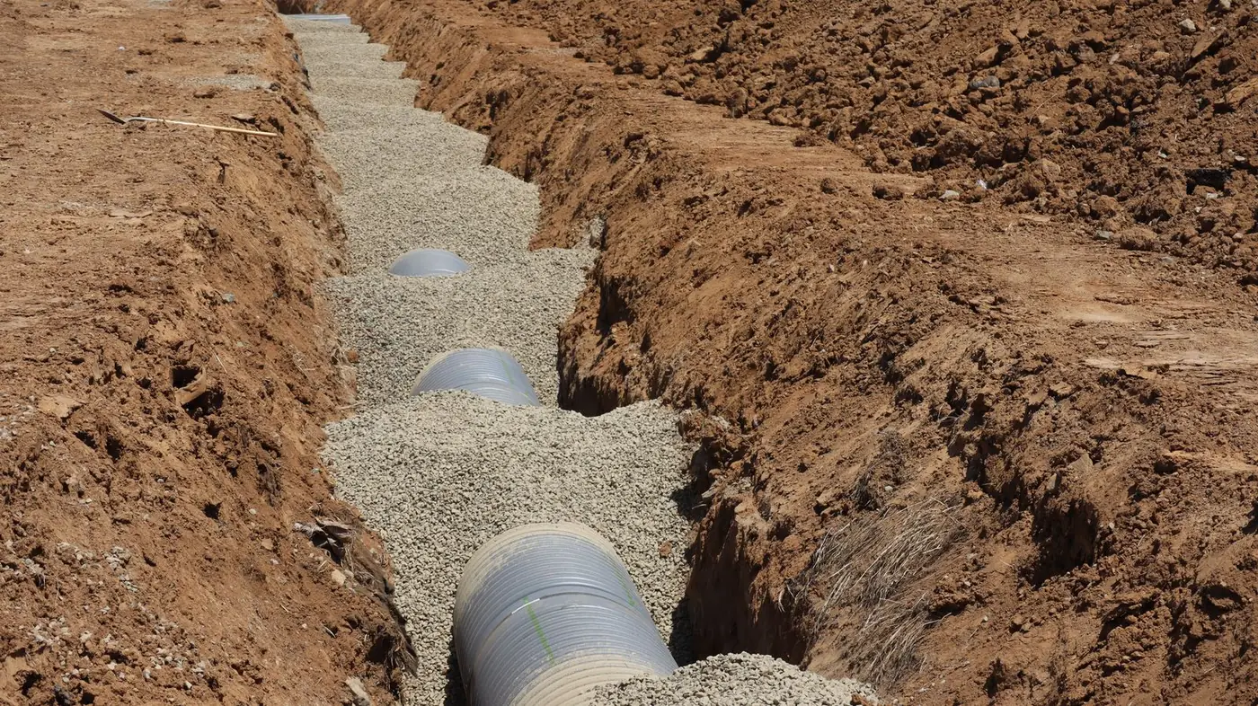 Septic drainfield line laid in a gravel-bedded trench through North Texas red clay during a system installation